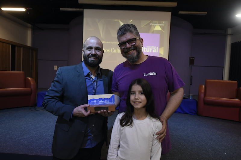 O Diretor Executivo da Guarulhos Cultural, Vitor Souza, juntamente com sua filha Lorena Buzato, recebem o Prêmio Prêmio Luis Figueira de Quental 2022 na Categoria Comunicação das mãos do Diretor de Turismo de Guarulhos, Ricardo Balcone.